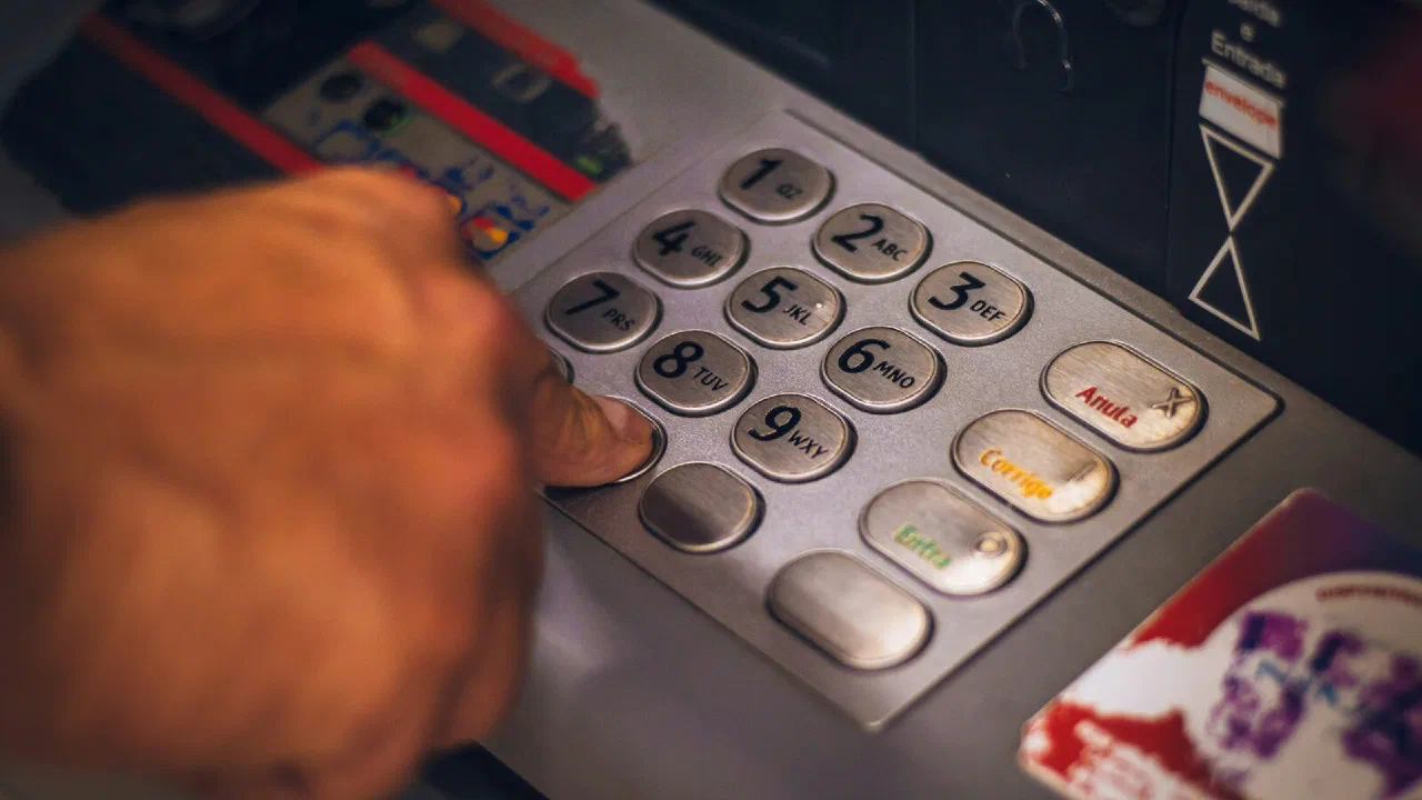 A hand pressing a button on a metallic ATM keypad