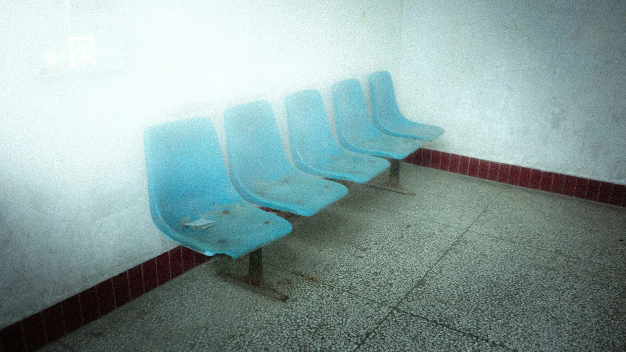 A row of empty blue plastic chairs along a wall in a waiting room