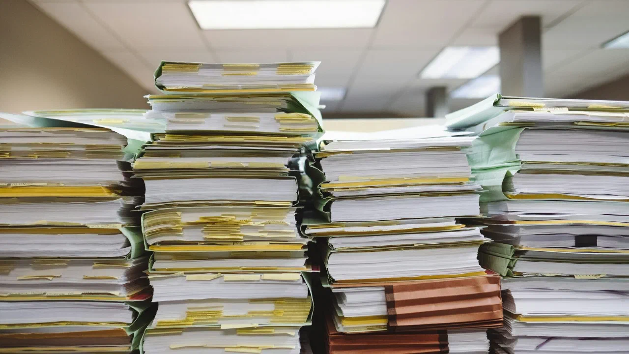 Stacks of loose paper documents and file folders piled on a surface