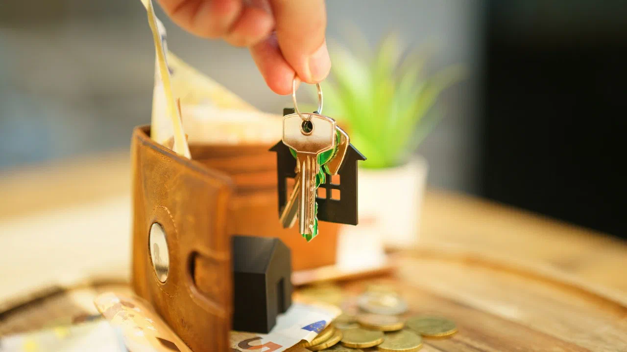 A hand holding door keys with a house charm and a wallet