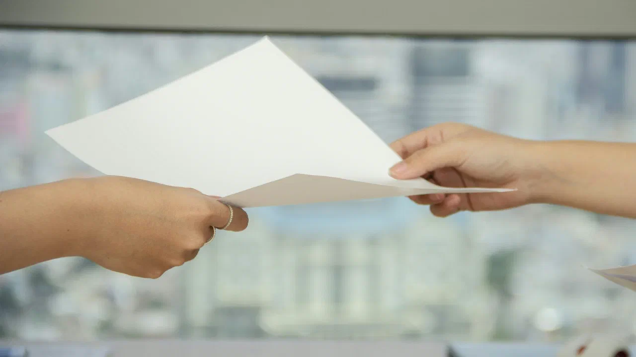 One person handing a sheet of paper across a desk to another